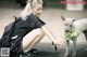 A woman kneeling down next to a dog with a plant in its mouth.