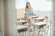 A woman in a white bikini holding a book in a classroom.