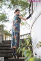 A woman in a blue dress and black gloves leaning against a wall.