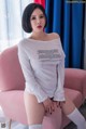 A woman sitting on a pink chair wearing a white shirt.