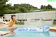 A woman in a yellow bikini jumping into a swimming pool.