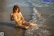 A woman in a yellow bikini sitting on the beach.