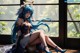 A woman with long blue hair sitting on a window sill.