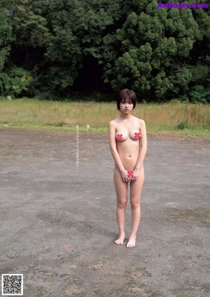 A naked woman standing in the middle of a dirt road.