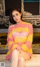 A woman sitting on a couch wearing a pink and yellow sweater.